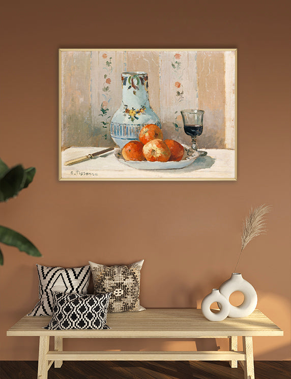 Framed still life painting on a wall above a wooden bench with decorative pillows and vases.