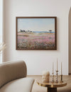 Framed landscape painting on a wall above a table with decorative items in a living room.