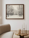 Framed winter landscape print on a wall above a sofa and side table with candles.