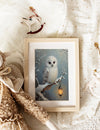 Framed picture of an owl on a branch with a lantern, surrounded by soft textures and neutral colors.