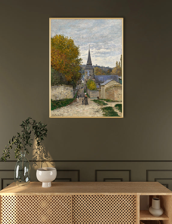 Framed painting of a village scene on a dark wall above a wooden console table.