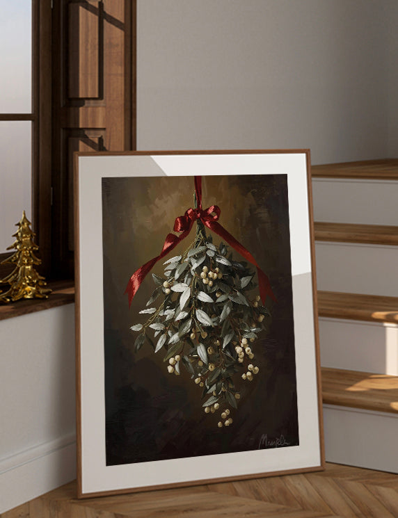 Framed artwork of a mistletoe hanging with a red ribbon on a wall.