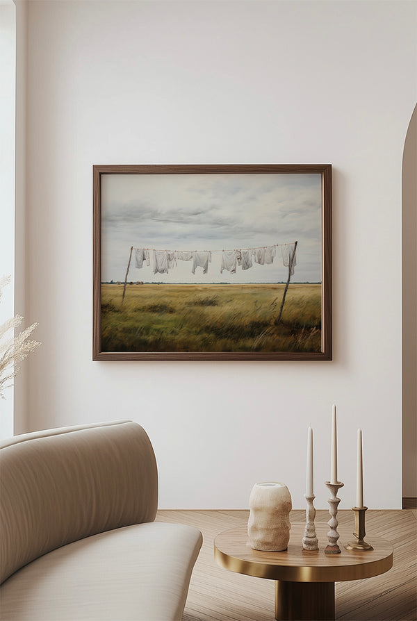 Framed artwork of a landscape with a field and clothesline on a wall above a sofa.