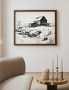 Framed black and white landscape print of a snowy scene with a wooden cabin on a wall above a sofa.