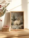 Framed artwork of a rabbit in a snowy landscape with a wrapped gift beside it on a wooden surface.